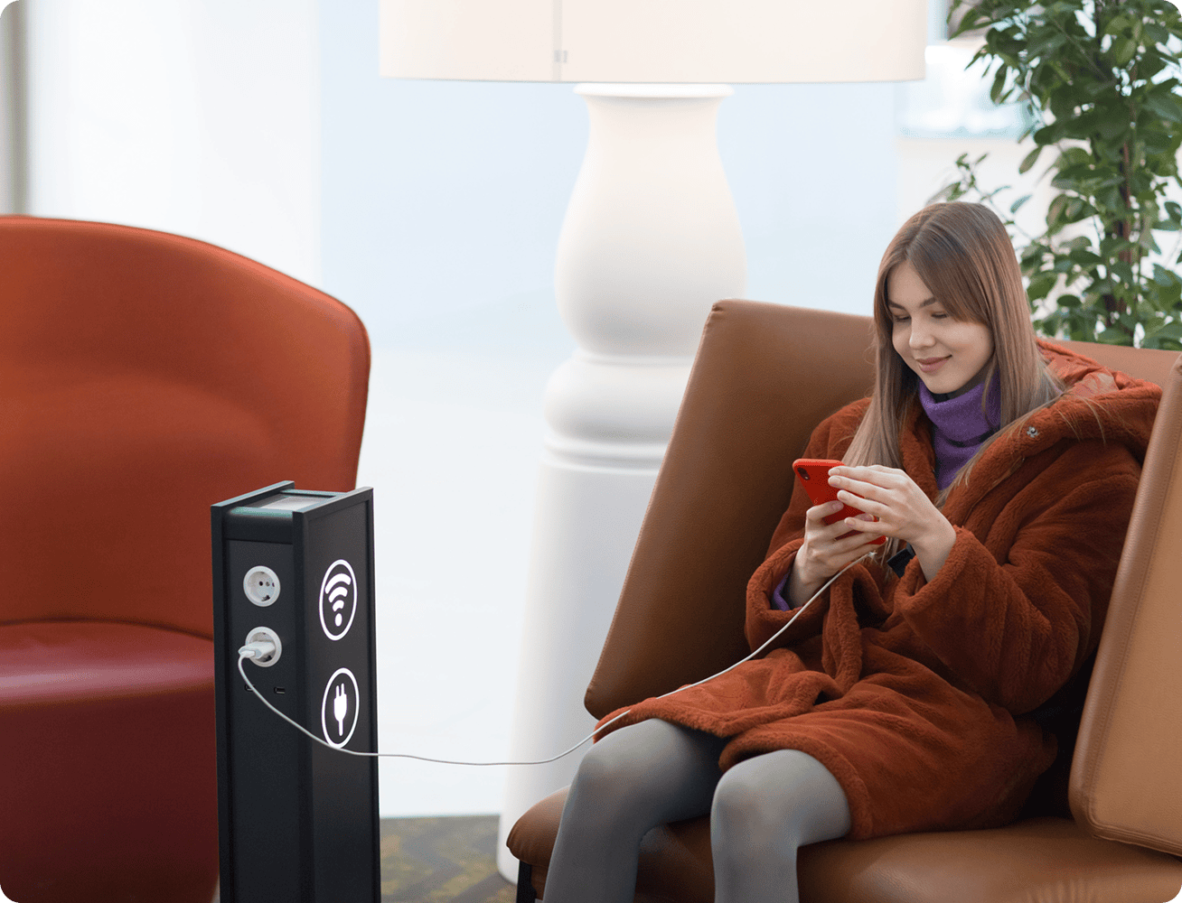 Woman charging phone in cozy cafe chair.